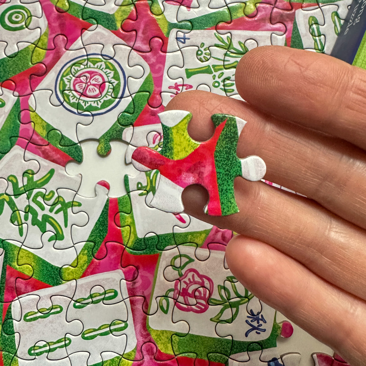 Hand holding a puzzle piece with a colorful design, surrounded by a partially completed puzzle.