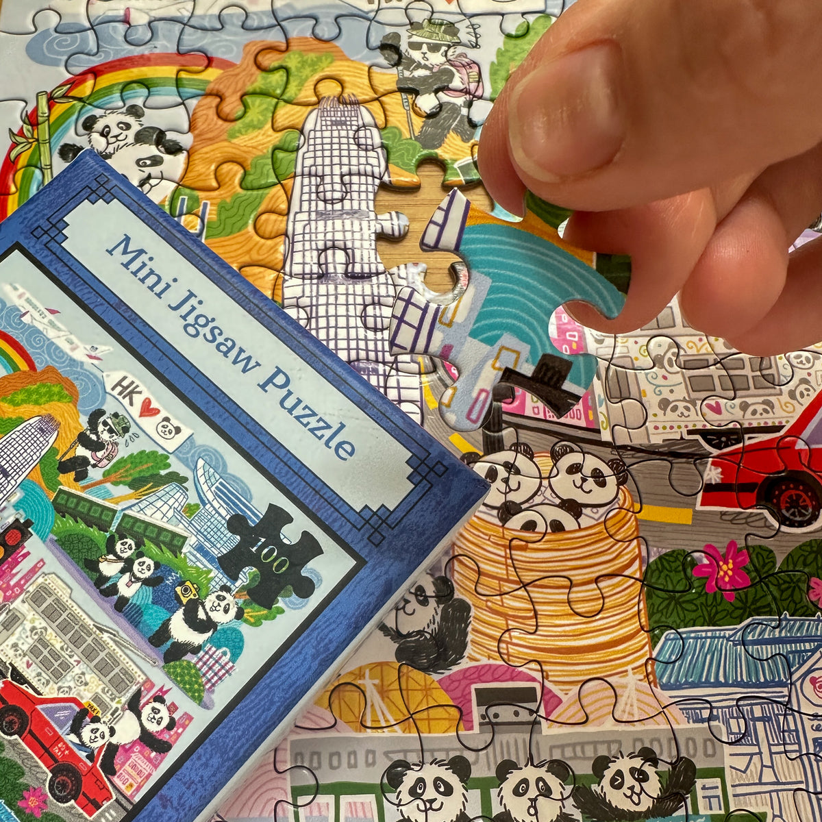 Mini jigsaw puzzle with panda design and a hand holding a piece.