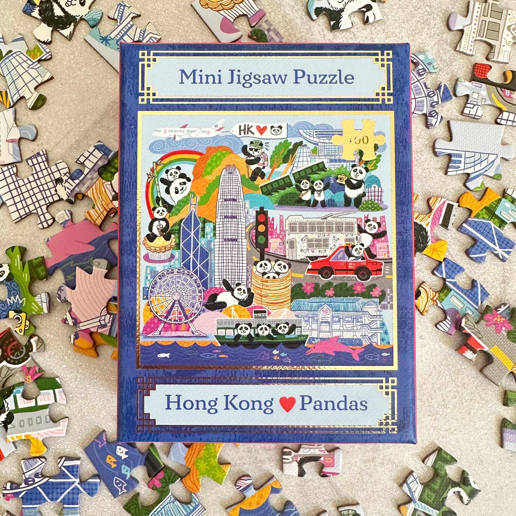 Mini jigsaw puzzle box with Hong Kong and panda design surrounded by scattered puzzle pieces.