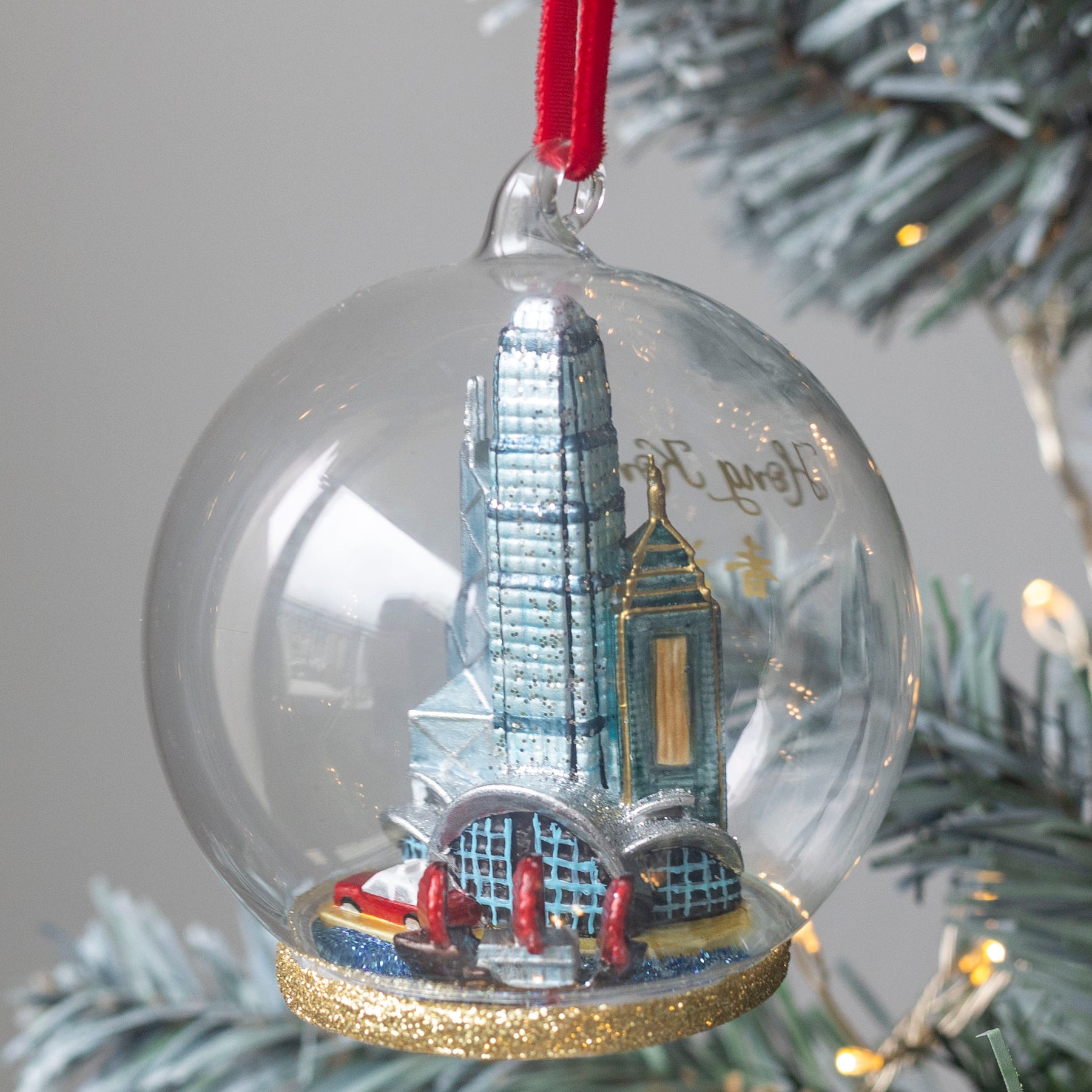 Glass Christmas ornament with a Hong Kong cityscape and taxi inside, hanging on a tree 