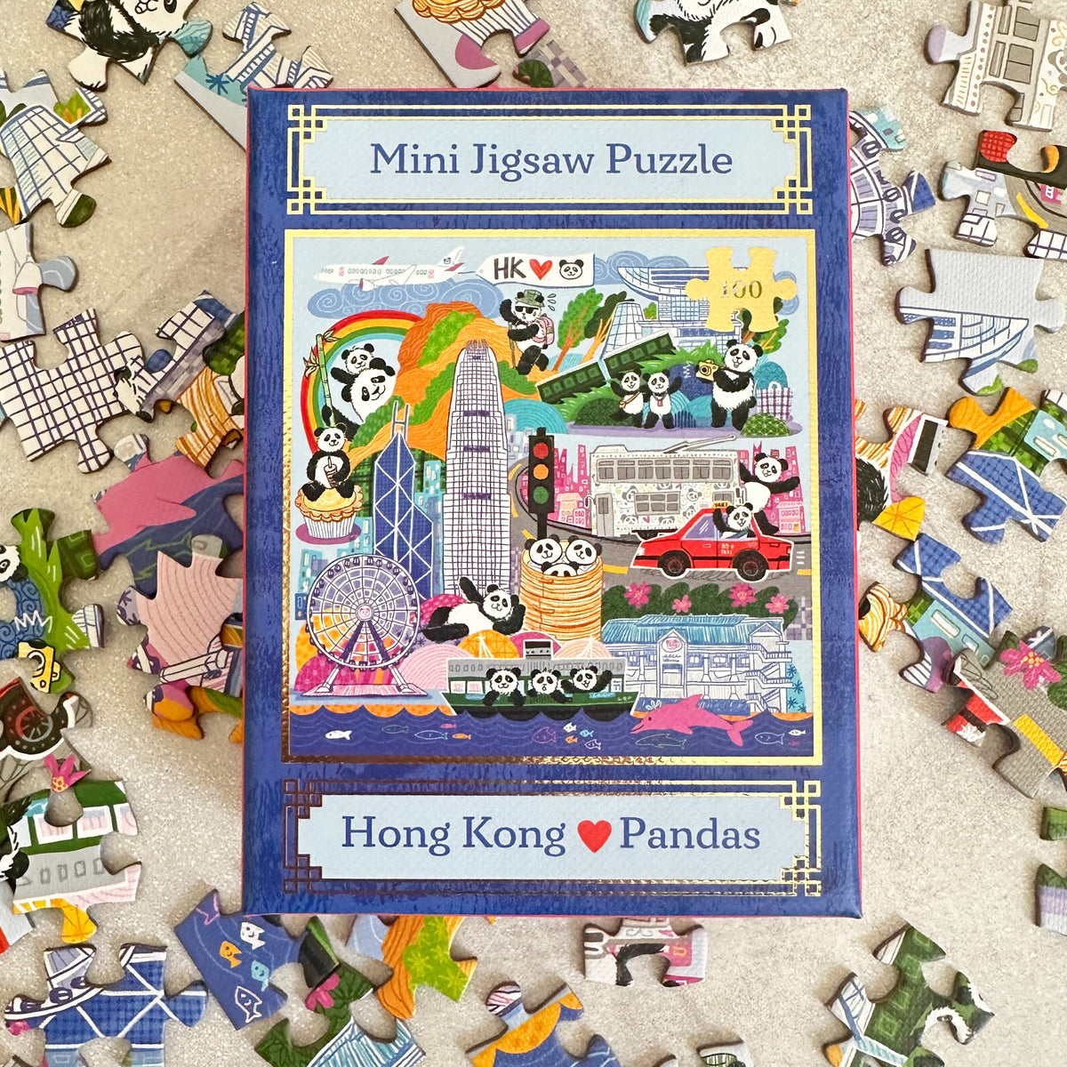 Mini jigsaw puzzle box with Hong Kong and panda design surrounded by scattered puzzle pieces.