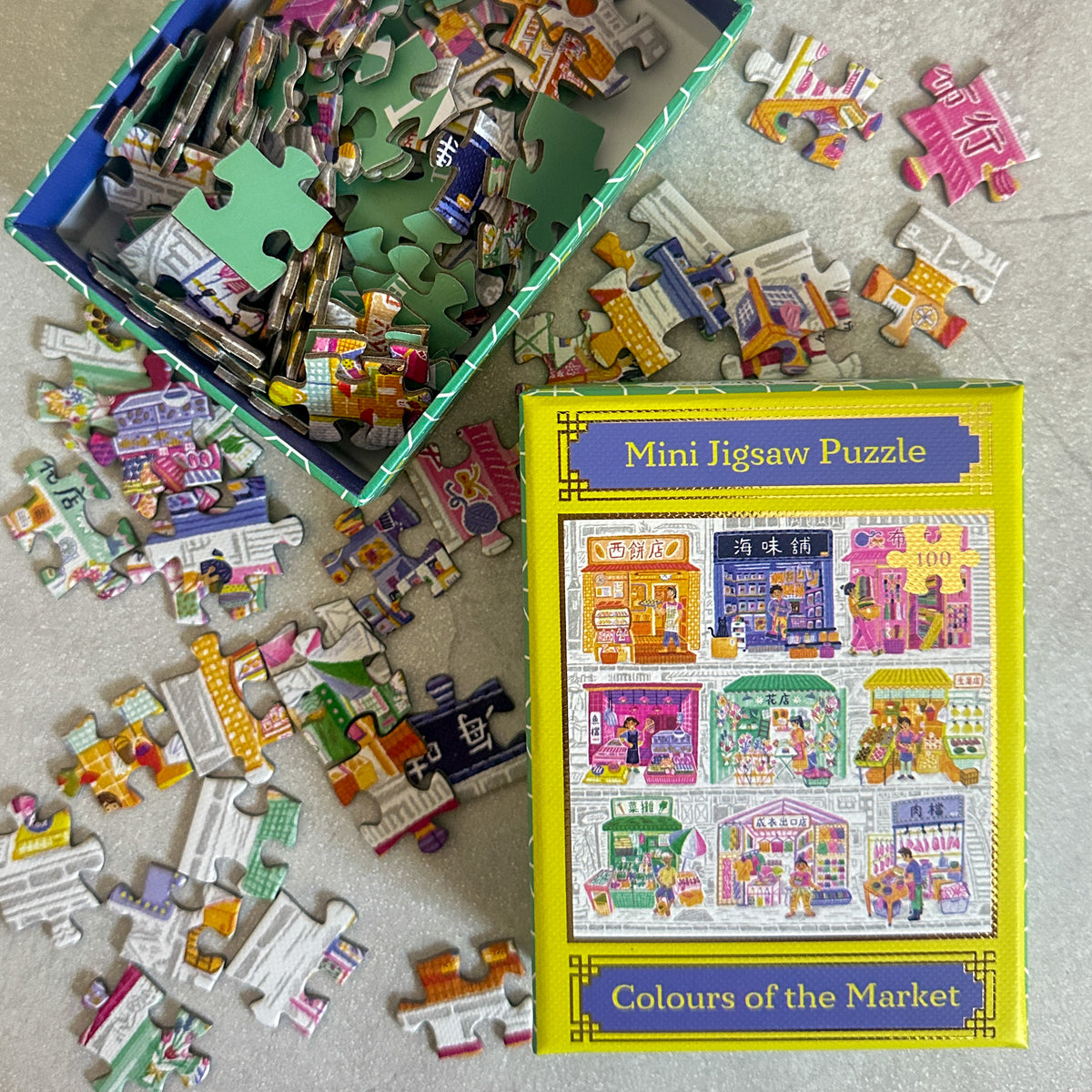 Mini jigsaw puzzle with pieces scattered on a surface, featuring a colorful market scene in Hong Kong box design.